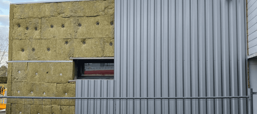 Pose d’un isolant en laine minérale et bardage métallique dans le cadre d’une isolation thermique par l’extérieur (ITE) sur bâtiment tertiaire.