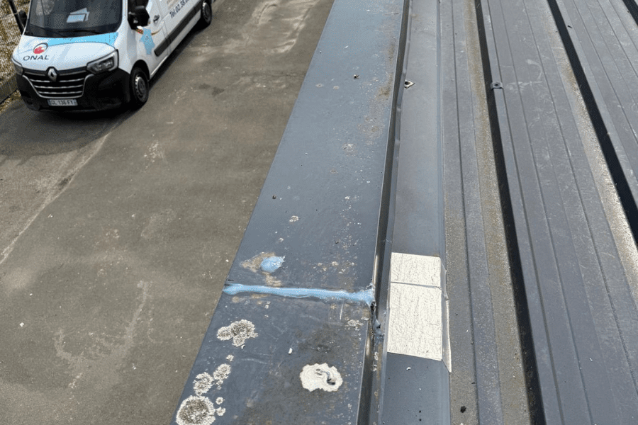 Toiture en bac acier montrant des réparations au mastic et des zones d’usure, avec un véhicule de l’entreprise ONAL visible en arrière-plan.